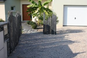 Aménagement d'une allée devant une maison avec des graviers, des paravents en pierres et des dalles devant la porte d'entrée par Aux 1001 Saisons